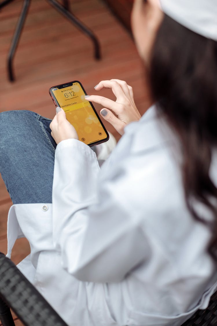 Person In White Long Sleeves Swiping The Cellphone She Is Holding