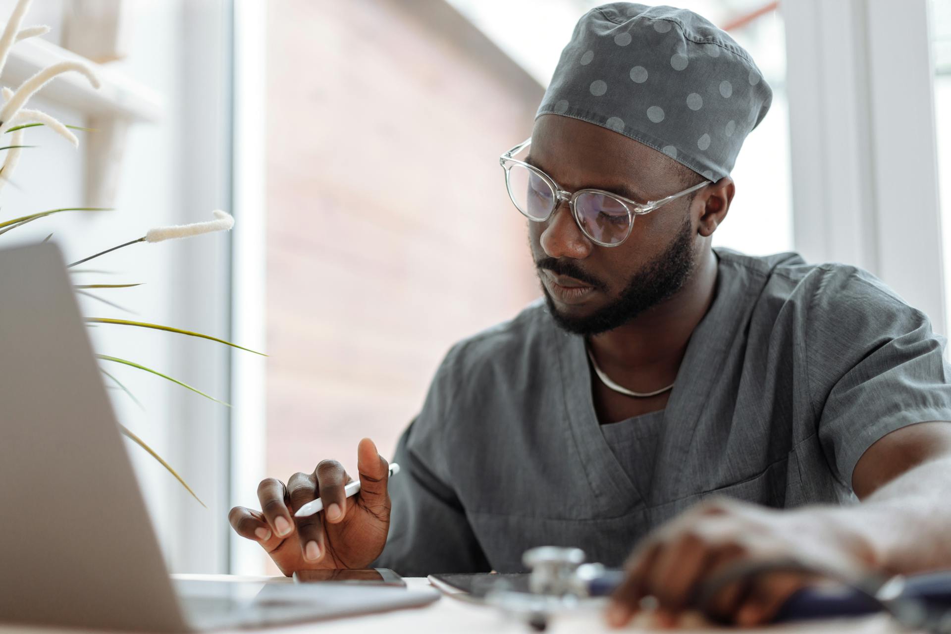 A focused male doctor in scrubs working on a laptop, showcasing professionalism and modern healthcare technology.