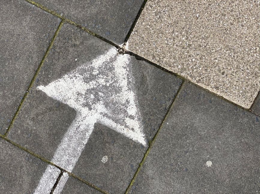 A white arrow painted on a concrete pavement in Gosforth, England.