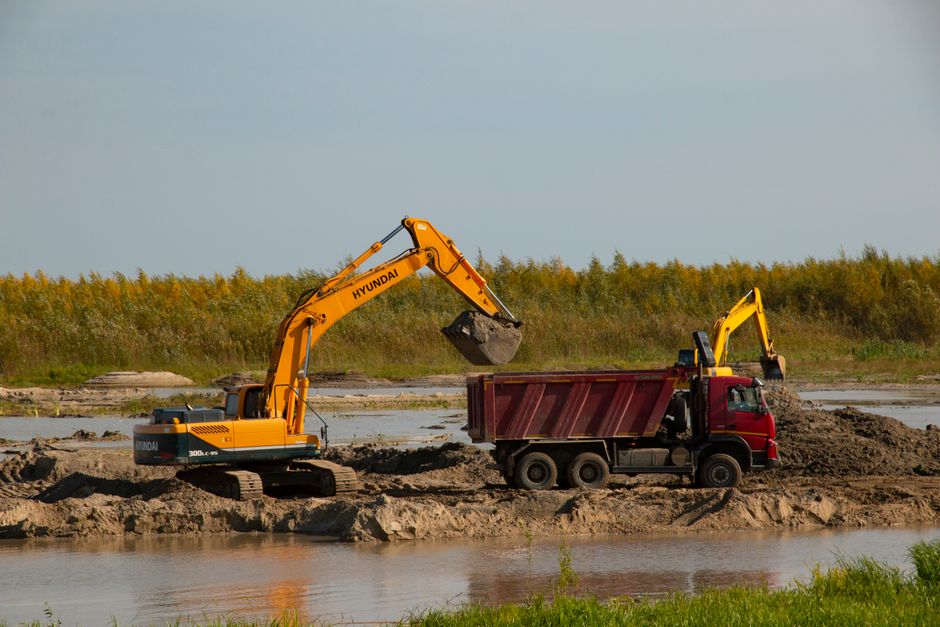 Excavator transfers soil to a dump truck by a river at a construction site. Machinery in action. Excavator transfers soil to a dump truck by a river at a construction site. Machinery in action.