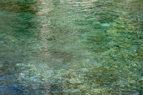 From above of crystal clear water of lake with stones rippling surface and stony bottom
