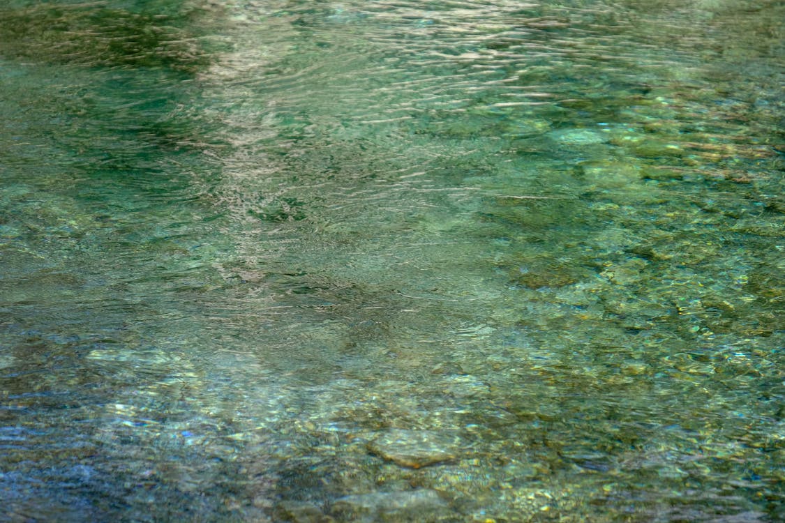 From above of crystal clear water of lake with stones rippling surface and stony bottom