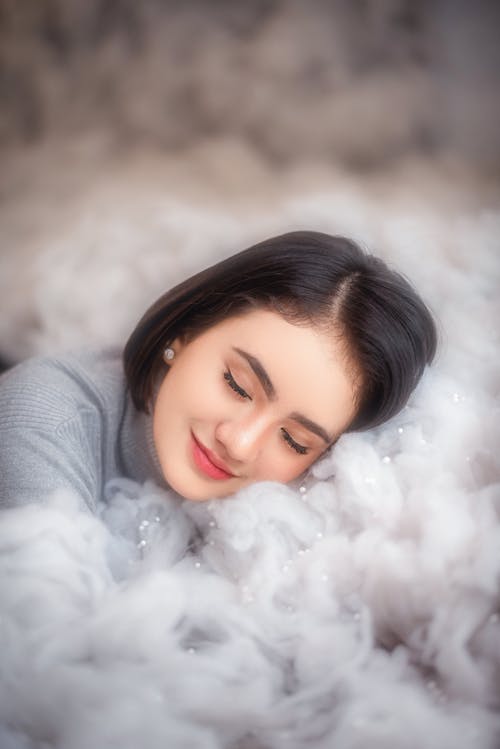 High angle of dreamy young female lying on soft fur blanket with closed eyes and smiling