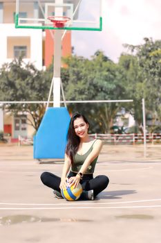 Asian woman smiling with volleyball on a sunny basketball court