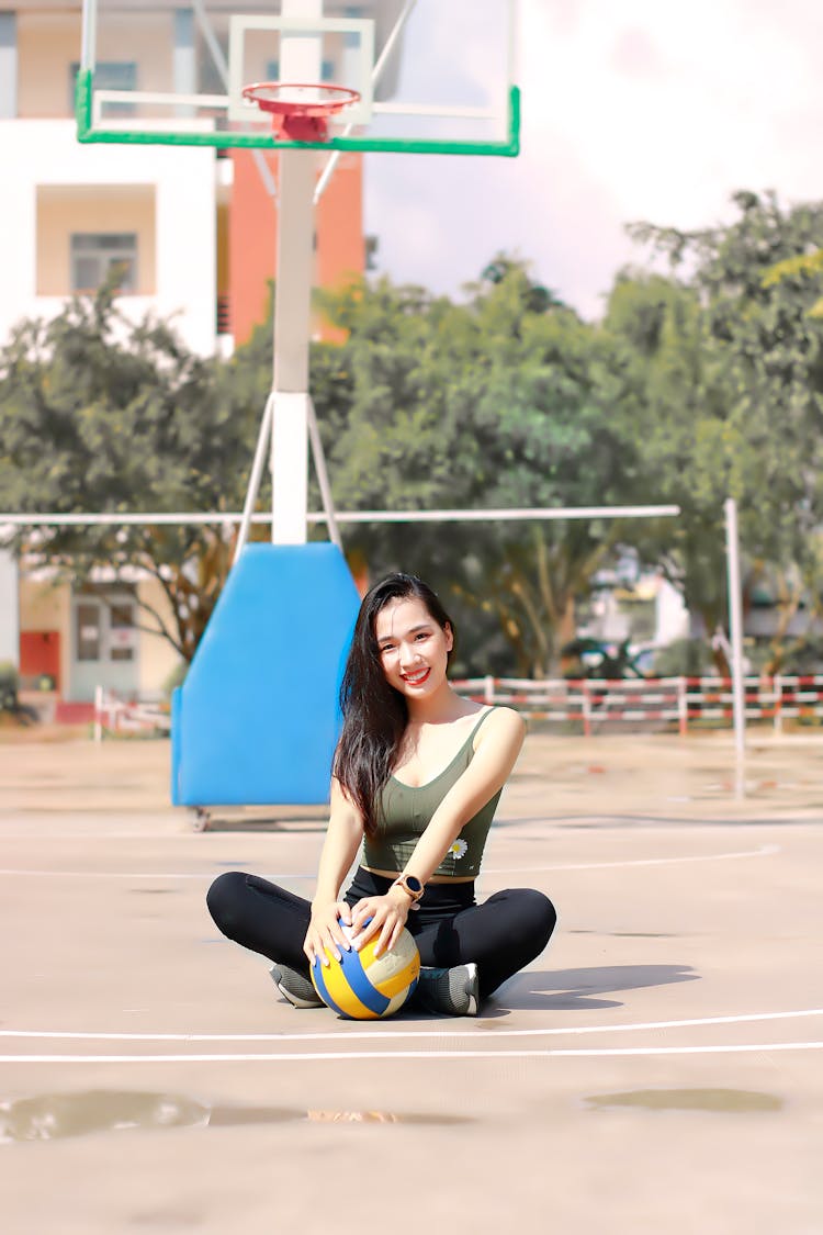 Asian Woman Sitting On A Court Holding A Volleyball Ball 