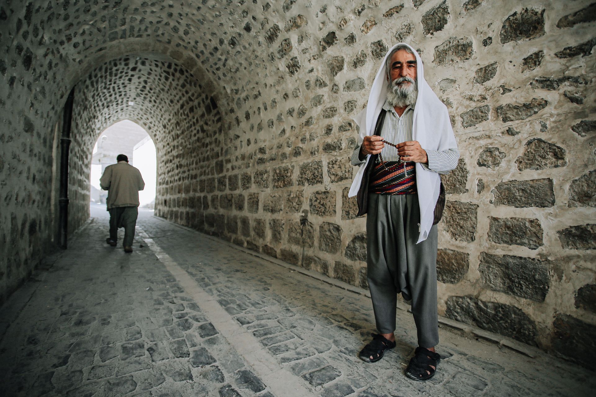 Ethnic bearded man with prayer beads near rough temple wall