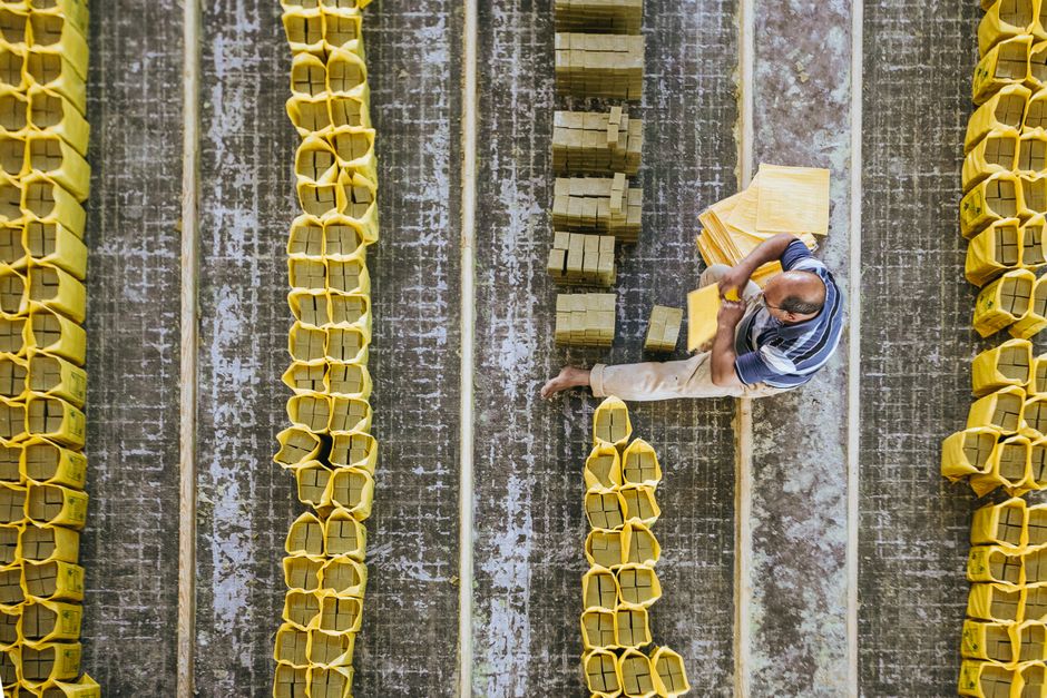 Top view of anonymous barefoot male worker sitting on floor while putting hard soap into plastic packages in production room
