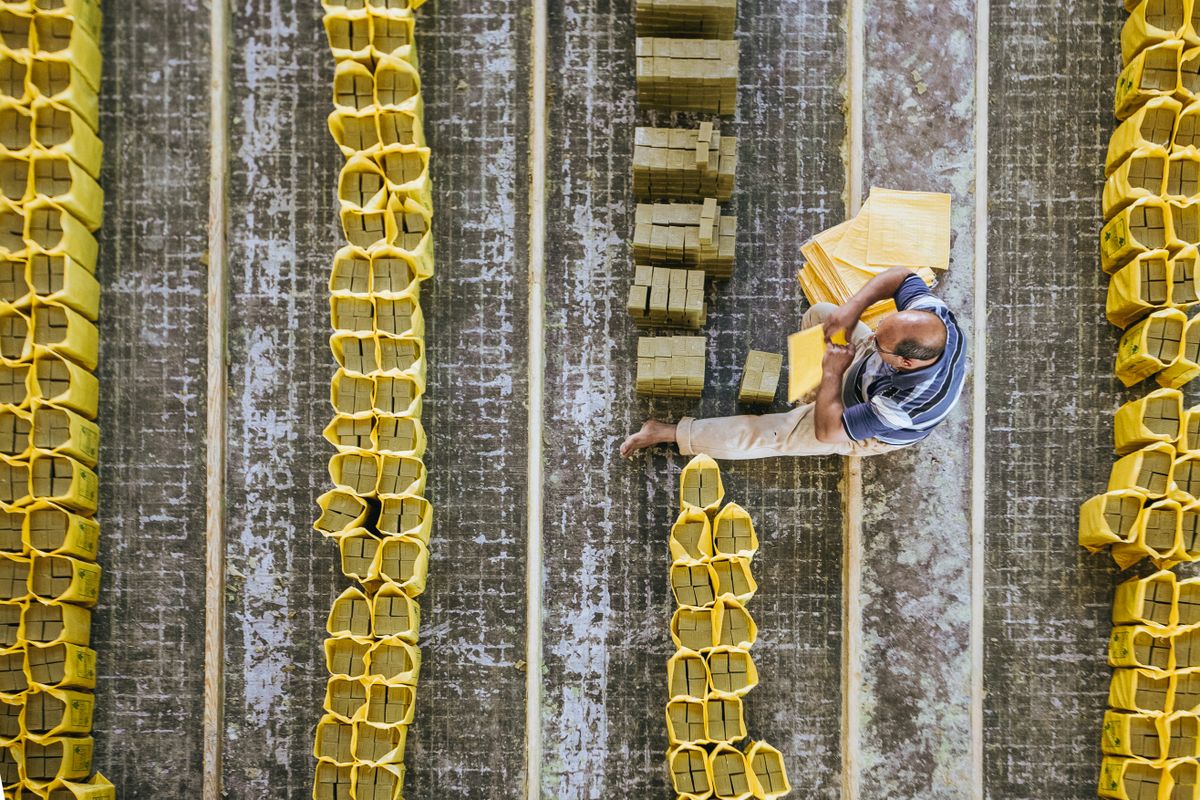 Top view of anonymous barefoot male worker sitting on floor while putting hard soap into plastic packages in production room
