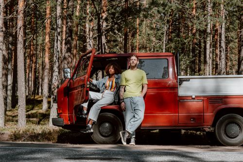 Free Young couple enjoying a road trip in a forest with their classic red pickup truck parked by the roadside. Stock Photo
