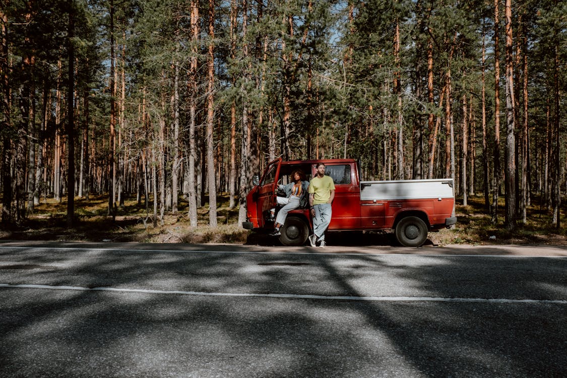Free Red and White Pick Up Truck Parked on Road Surrounded by Trees Stock Photo