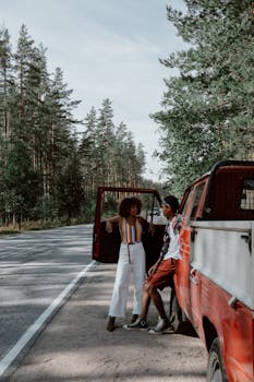 A young couple enjoys a roadside break by a red pickup truck surrounded by tall trees.
