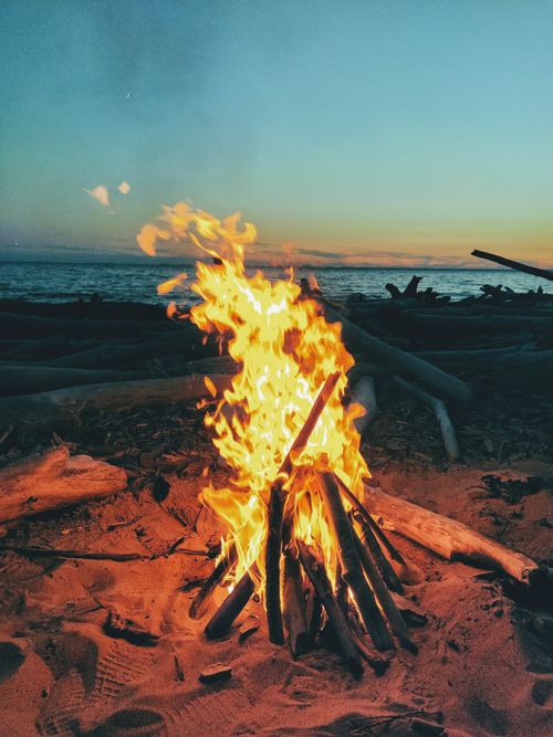 Free A captivating beach bonfire with glowing flames at sunset near the ocean, ideal for outdoor and adventure themes. Stock Photo