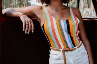 一名年轻女子身着充满活力的条纹上衣和白色短裤，在户外倚靠在车上