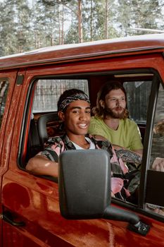 Two young men smiling in a red vehicle on a sunny day, ready for adventure.