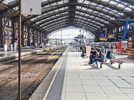 Commuters seated and waiting in Lille's historic train station with an arched glass roof.