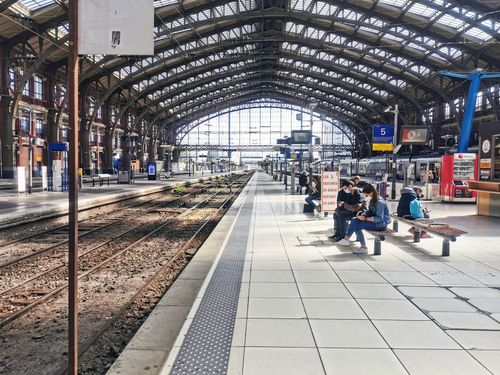 Free Commuters seated and waiting in Lille's historic train station with an arched glass roof. Stock Photo