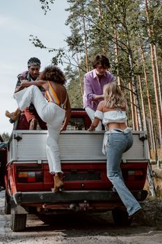 Four friends climb into a pickup truck on a sunny day, surrounded by nature.