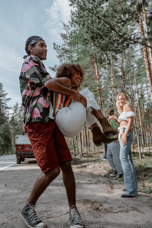 Man in Green and Black Shirt Carrying Woman in White Pants