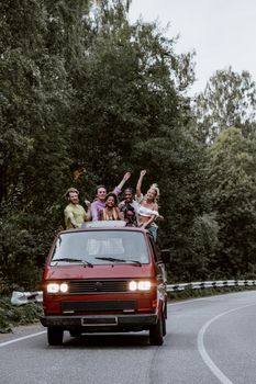 A diverse group of friends having fun on a road trip in a vintage van through a scenic forest.