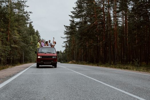 一群朋友站在森林道路旁的红色货车里，在公路旅行中玩得很开心
