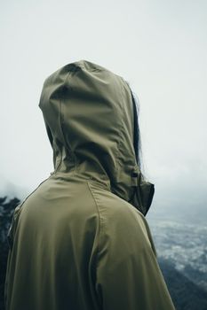 一个穿着绿色连帽衫的人俯瞰着朦胧的风景，心中涌起孤独与沉思