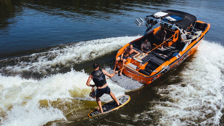 Anonymous Athlete On Wake Board On River Near Motor Boat