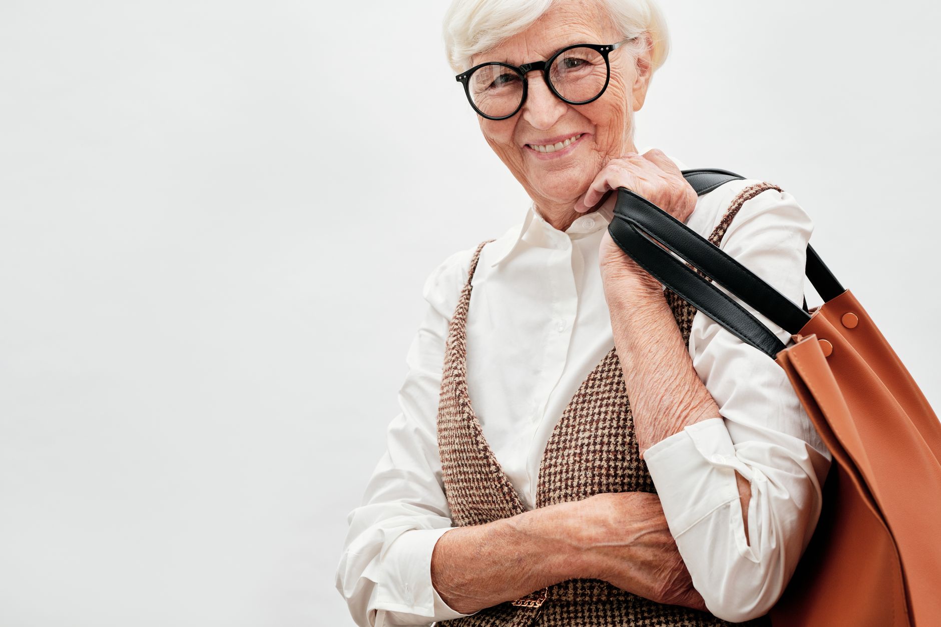 Chic senior woman in eyeglasses holding a shoulder bag, smiling confidently.