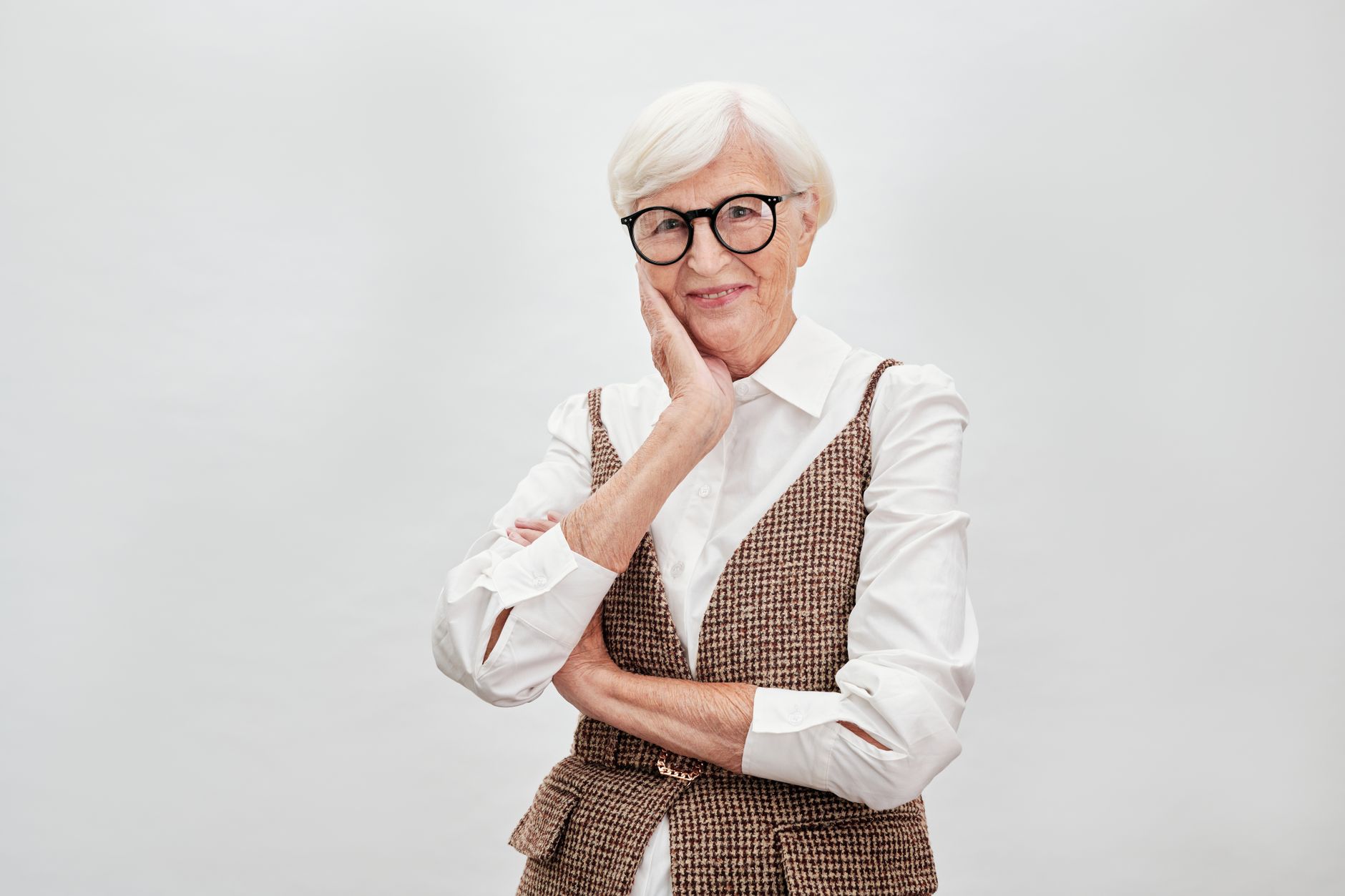 Elegant senior woman in eyeglasses posing confidently with a smile, wearing classic fashion.