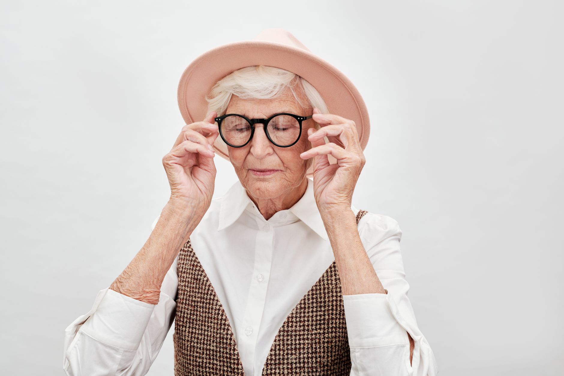 Stylish senior woman with eyeglasses and hat in a studio setting.