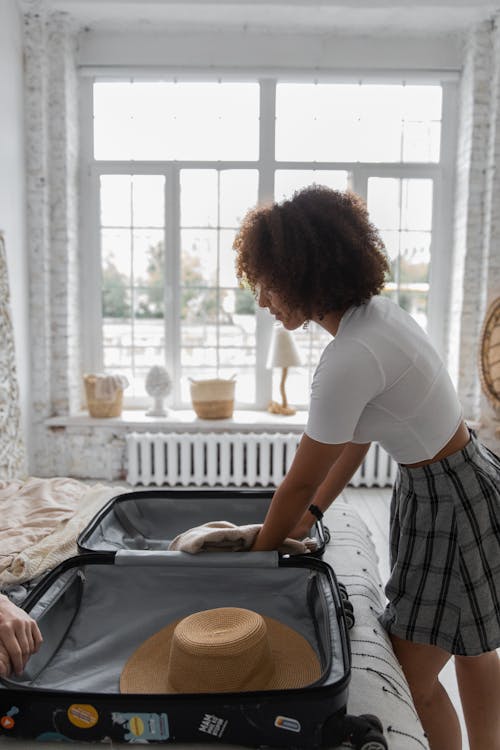 Side view of black female in casual clothes packing suitcase while preparing for trip at home