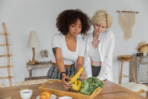 Loving multiethnic girlfriends in casual clothes standing near table while cooking breakfast together at home