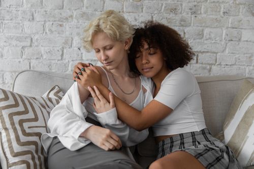 Free Multiethnic girlfriends in casual clothes chilling on couch at home while hugging each other with closed eyes Stock Photo