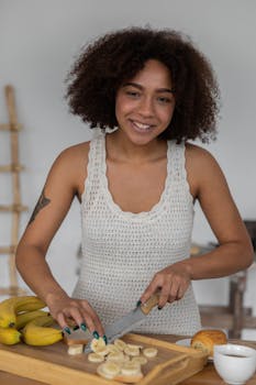 Smiling woman slicing banana for breakfast in cozy kitchen setting.