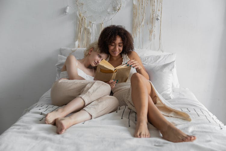 A Same Sex Couple Reading A Book While Lying On The Bed