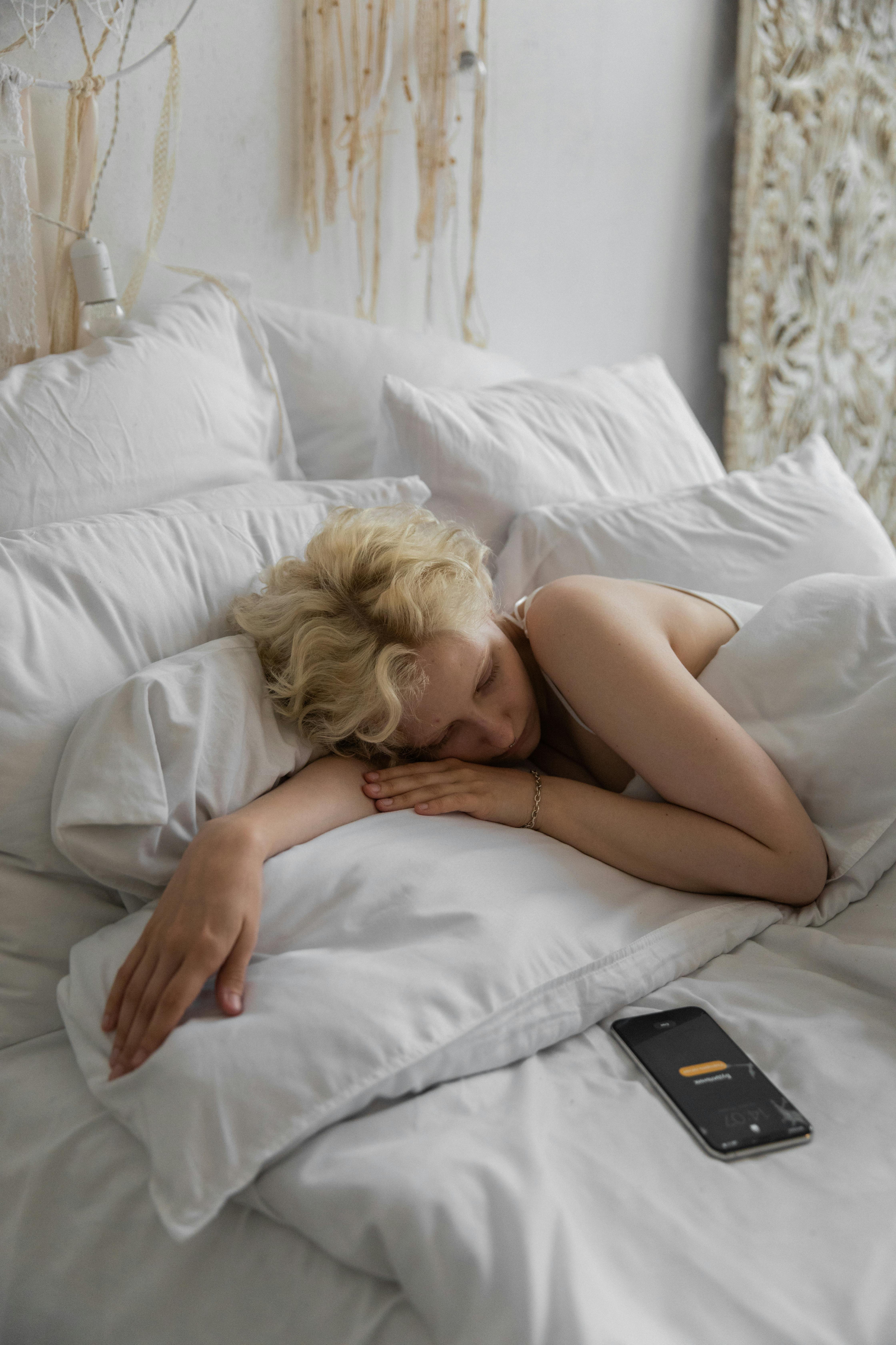 sleepy woman lying on bed with alarm on smartphone
