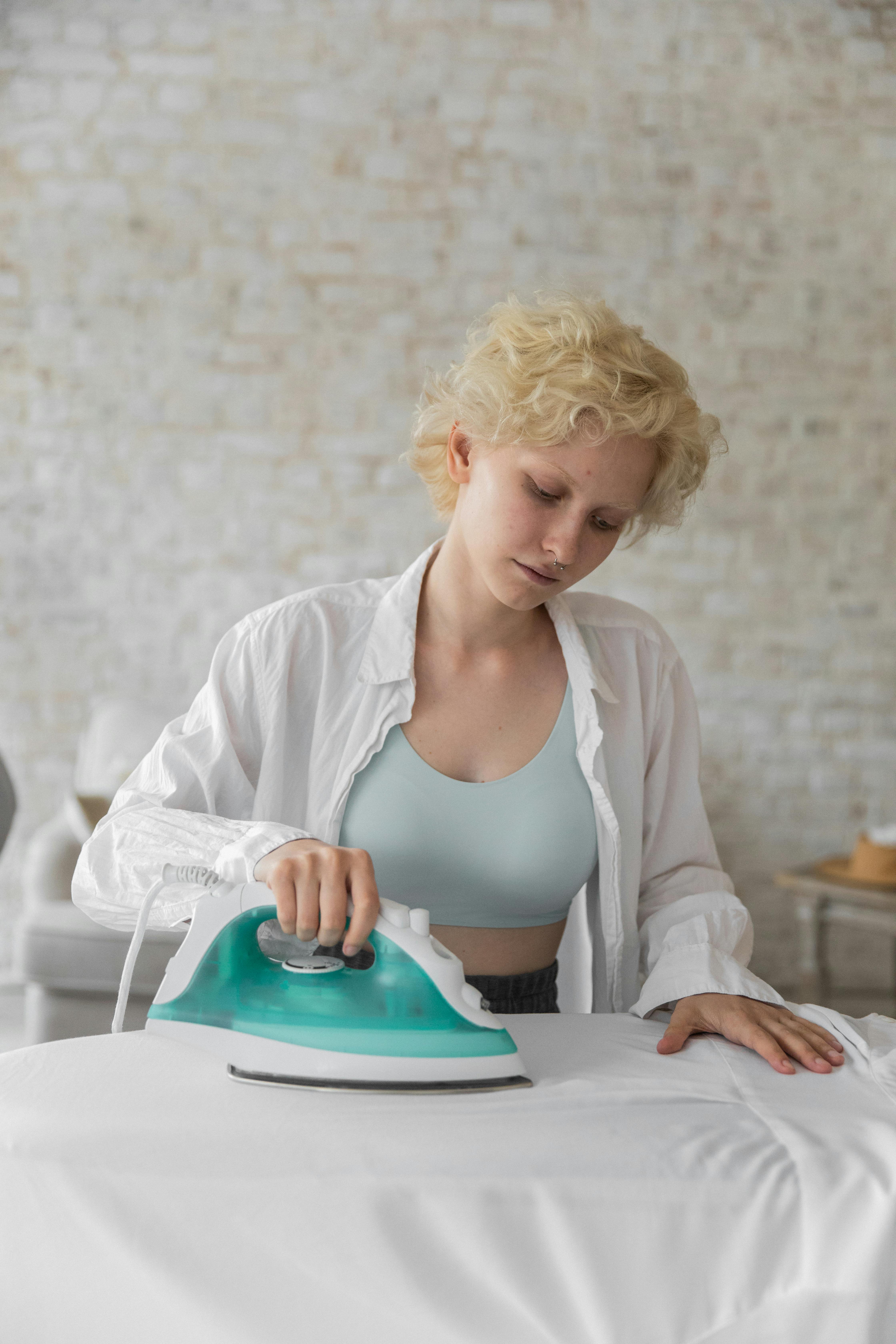serious woman ironing white clothes at home