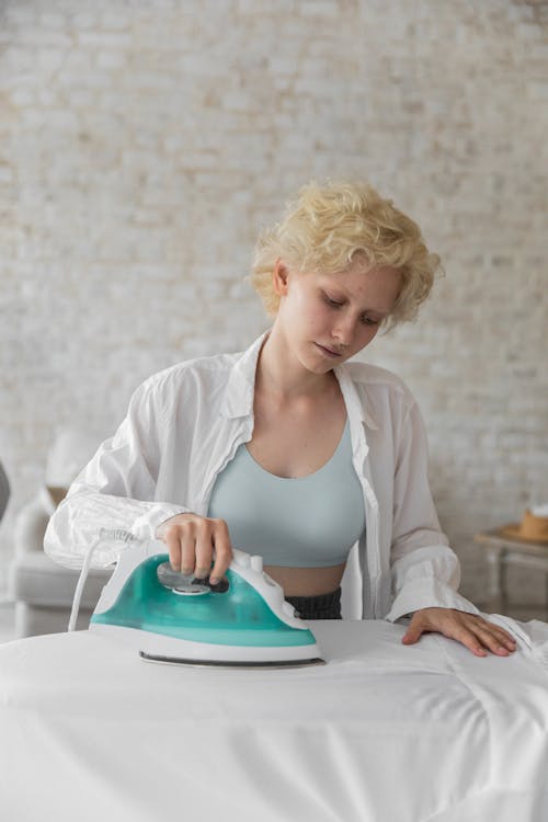 Free Serious woman ironing white clothes at home Stock Photo