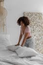 Awake African American female making bed in white bedclothes in bedroom in morning