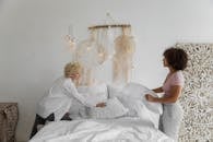 Side view of lesbian couple standing near comfortable bed and adjusting soft pillows in cozy bedroom