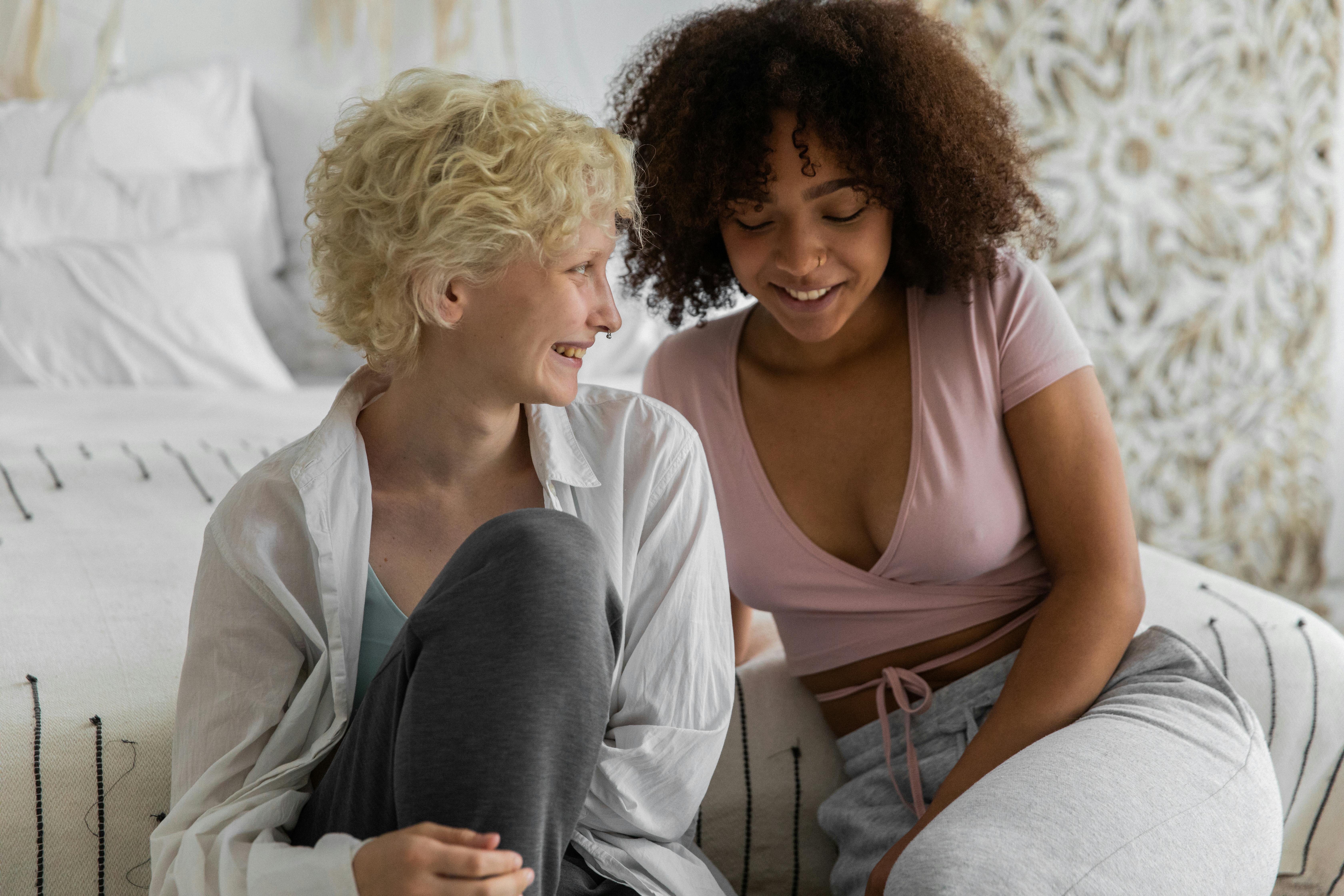 positive diverse girlfriends smiling while spending time together in bedroom