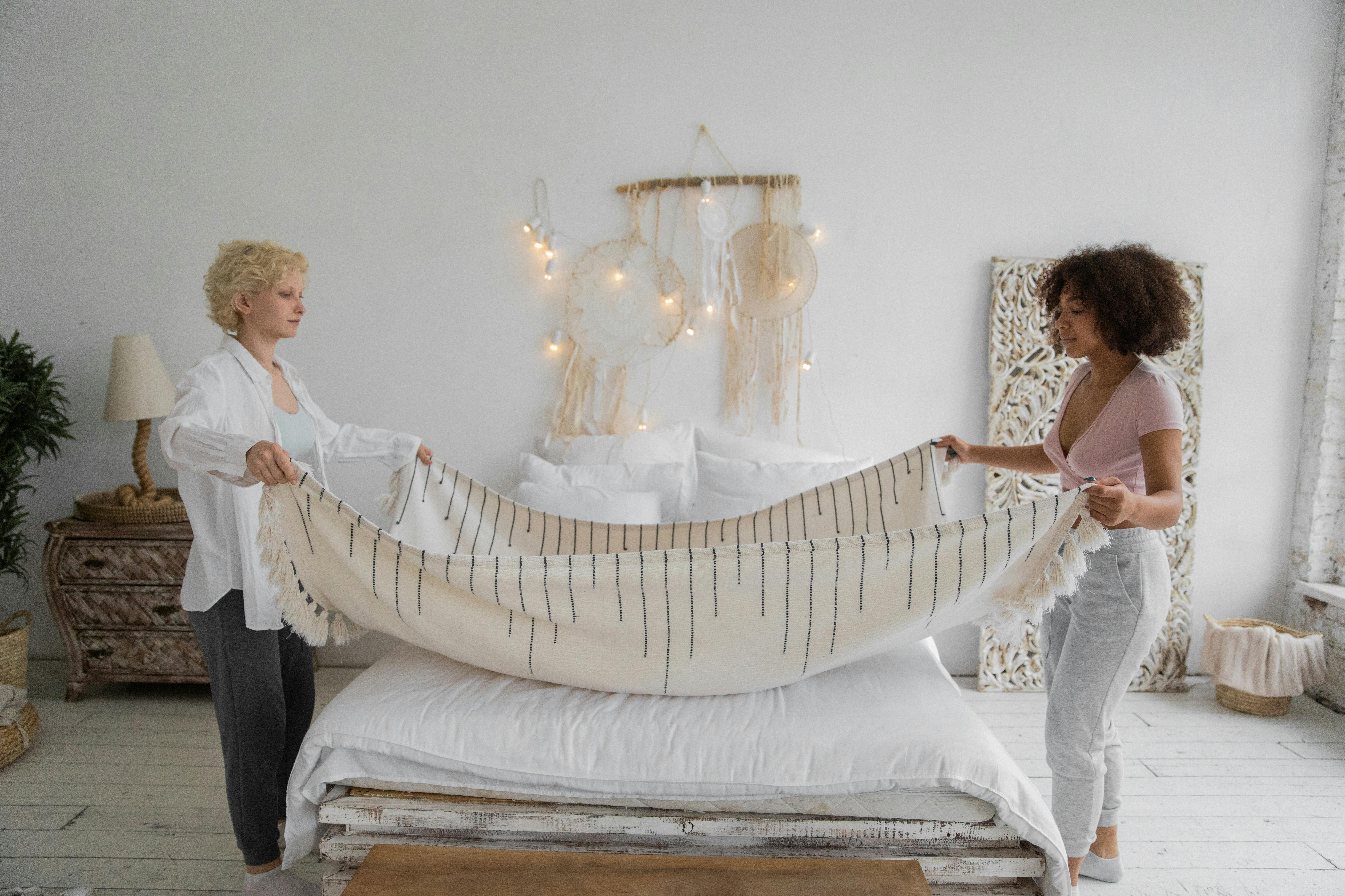 young multiracial women making bed in sunny morning