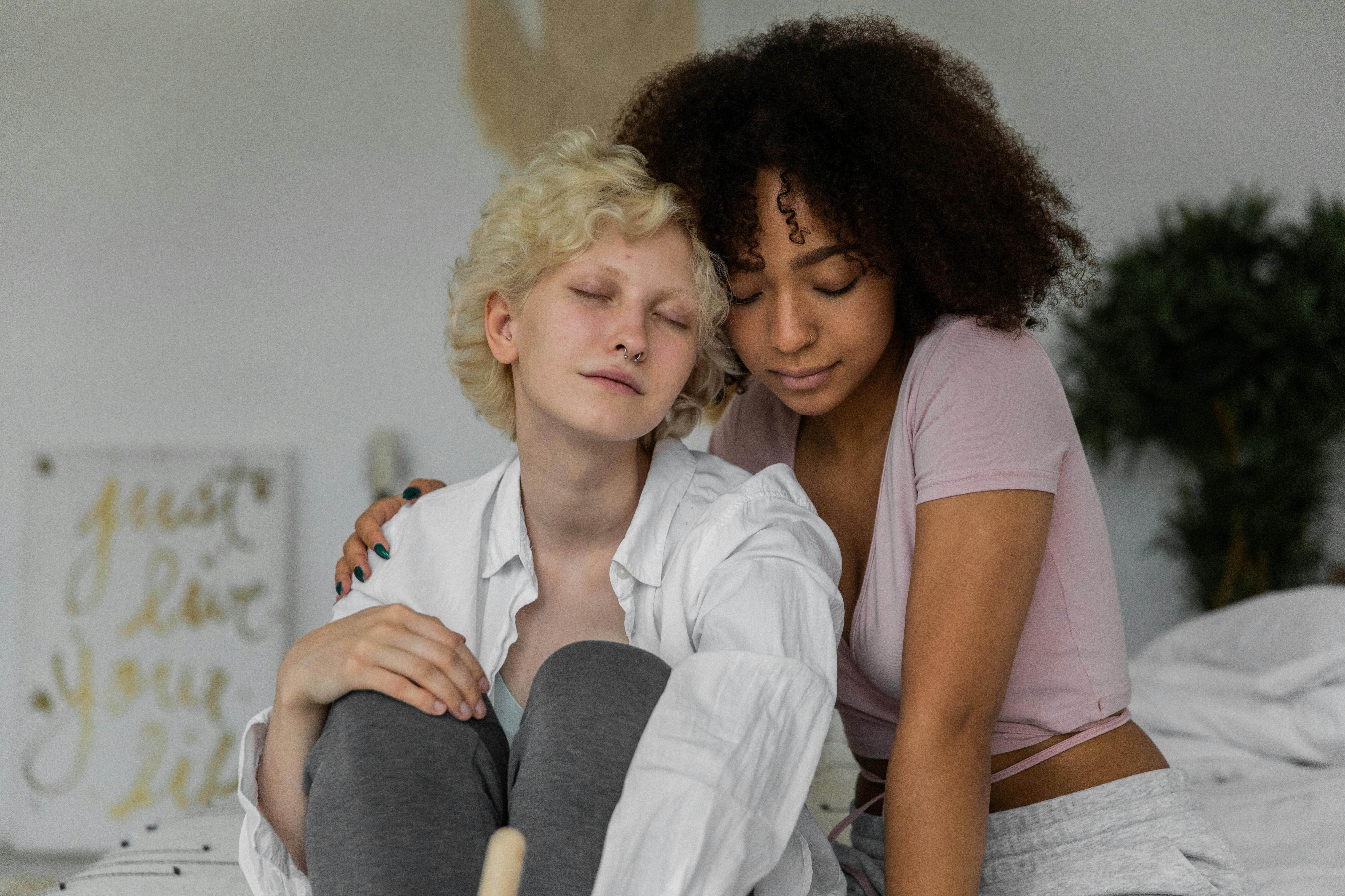 dreamy young diverse girlfriends hugging while resting together on bed