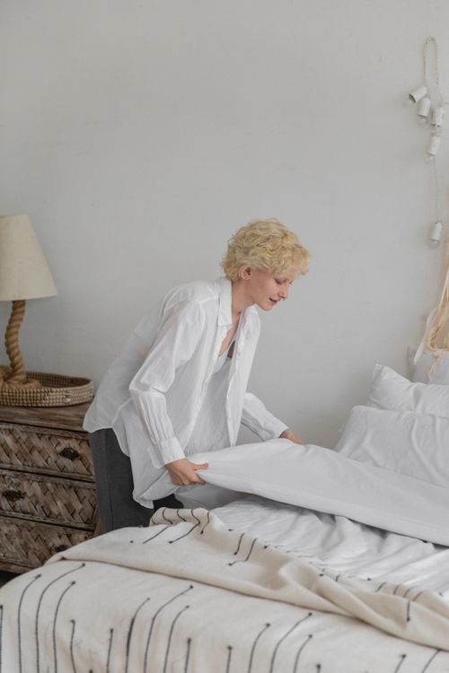 Free Side view of female in home clothing adjusting blanket while organizing bedroom during household routine Stock Photo