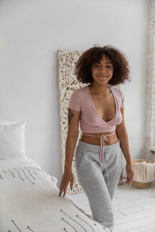 Free Positive African American female smiling widely standing near comfortable bed in cozy bedroom in morning Stock Photo