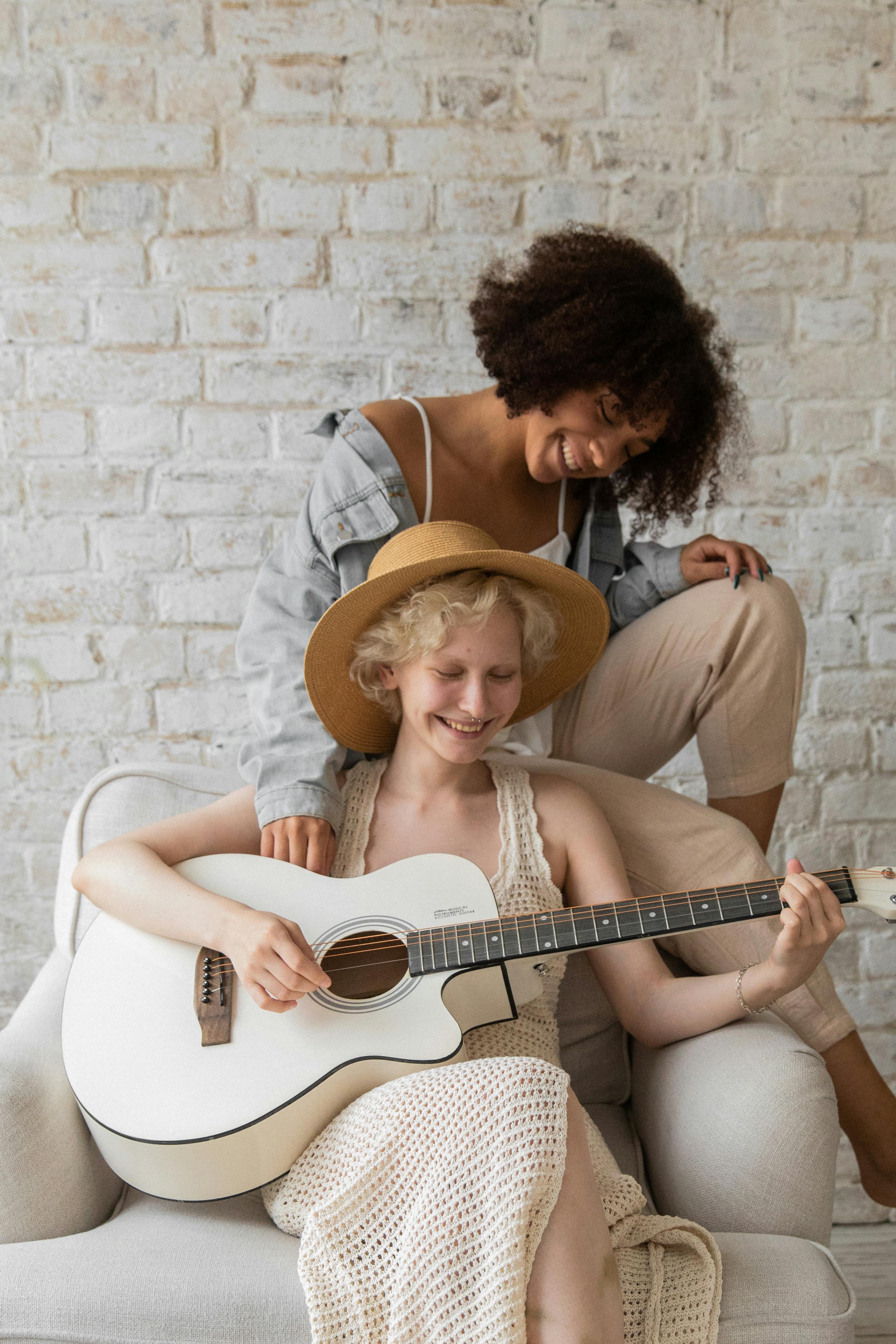 romantic multiethnic lesbian couple playing guitar at home