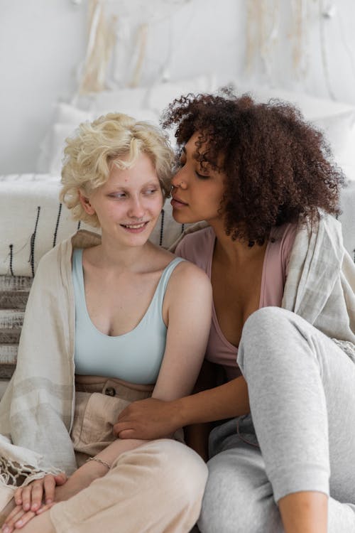 Peaceful young homosexual couple wrapped in plaid sitting close near bed in cozy apartment