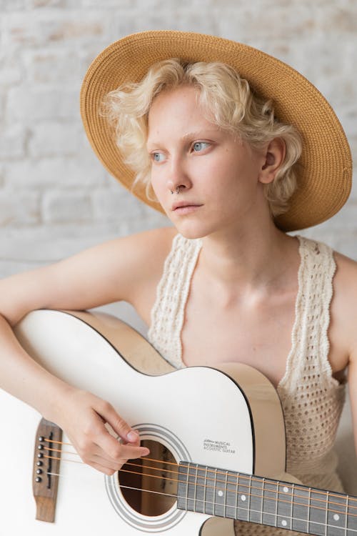 Stylish pensive young lady playing guitar against white brick wall