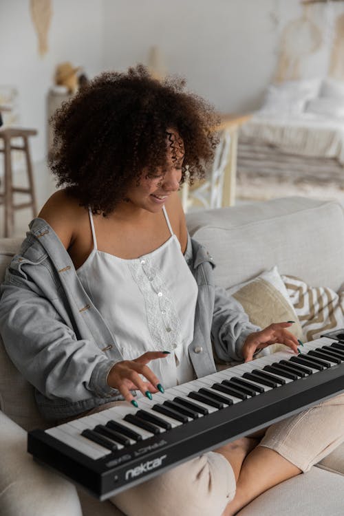 Glückliche Ethnische Frau, Die Synthesizer Spielt, Der Auf Couch Zu Hause Sitzt