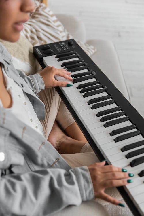 Crop ethnic lady playing synthesizer on sofa