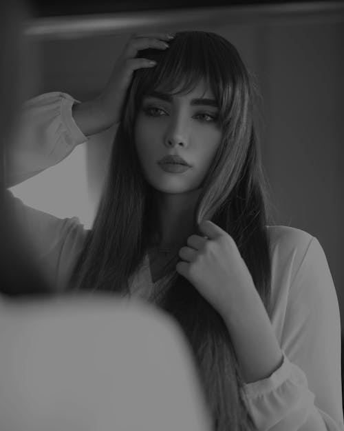 Black and white low angle of young pondering feminine lady in trendy wear touching hair and head while looking away